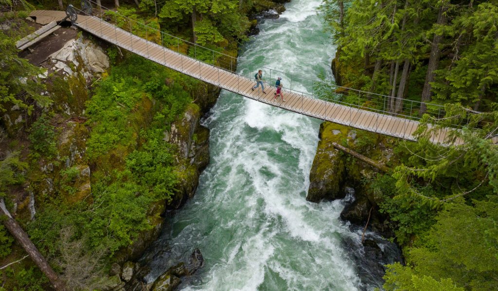 Three people walking on a bridge over a river.