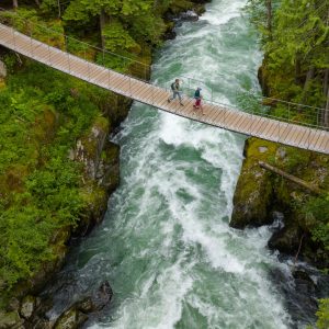 Three people walking on a bridge over a river.